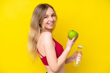 Blonde English young girl isolated on yellow background with an apple and with a bottle of water