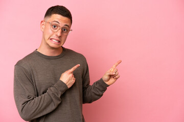 Young Brazilian man isolated on pink background frightened and pointing to the side