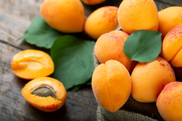 Ripe apricots and apricot leaves in a bag on a wooden background.