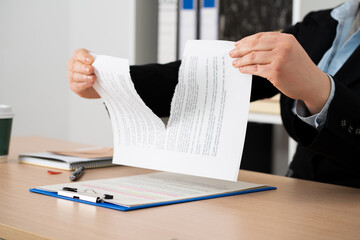 Close-up of the hands of a businesswoman tearing up the signed contract document sitting at a desk...