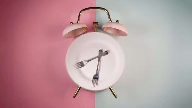 Alarm clock and a rotating plate with fork and knife. Time to eat, diet or Intermittent Fasting concept