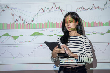 asian woman holding tablet standing in front of conference room presenting stock trading, gaming, business, investment, finance, background with projector projecting graphs in conference room