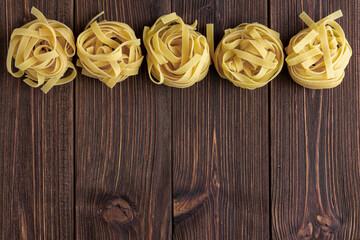 Raw pasta tagliatelle with copy space on wooden background.