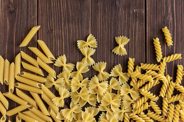 Different kinds of raw pasta texture with copy space on wooden background.