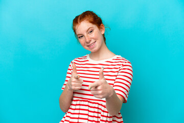 Young reddish woman isolated on blue background pointing to the front and smiling