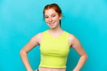 Fototapeta na wymiar Young reddish woman isolated on blue background posing with arms at hip and smiling