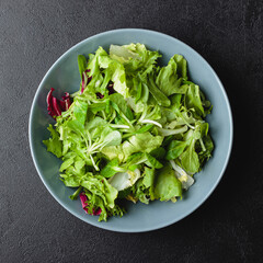 Green salad leaves in bowl on black table.