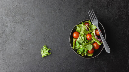 Green salad leaves in bowl on black table.