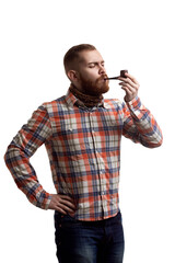Handsome bearded redhead guy in checked shirt smoking pipe while isolated on white background 