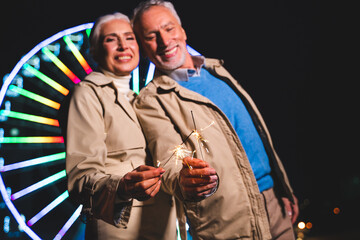 Beautiful senior couple bonding outdoors celebrating with fireworks in the night