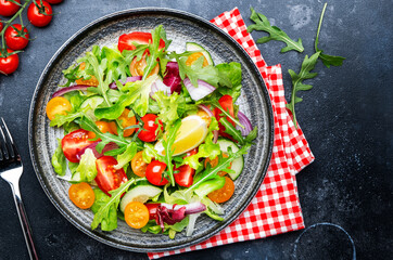 Fresh spring vegan vegetables salad with colorful cherry tomatoes, cucumber, red onion, lettuce, radicchio and arugula. Dark table background, top view