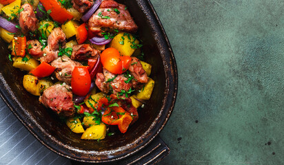 Turkey drumsticks roast with potatoes, paprika, onions, herbs and spices in rustic cast iron pan, old green table background, top view