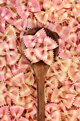 Farfalle pink striped bow tie pasta dyed with beetroot in an olive wood spoon. Healthy dried gourmet Italian food background concept. Top view, flat lay.