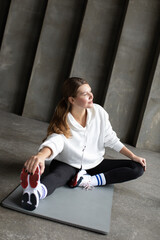 Fototapeta na wymiar An athlete in leggings, a hoodie and sneakers stretches the muscles of her legs before training