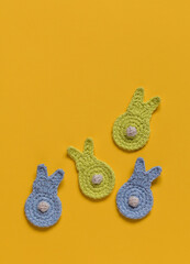 Blue yelow crochet bunnies with white tails on a yellow backgound. Happy Easter concept. Top view. Copy space.