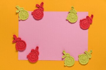 Easter compostion. Red yellow crochet bunnies and pink paper blank on a yellow background. Top view. Copy space.