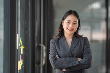 Fototapeta premium Beautiful Asian businesswoman standing with her arms crossed and confidently looking at the camera in the office.