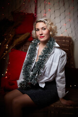 An elegant blonde girl in a white blouse in a room decorated for Christmas or new year with a background, tinsel and light garlands