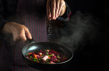 The cook adds salt to a steaming hot pan. Cooking fresh vegetables on the kitchen. Copy space