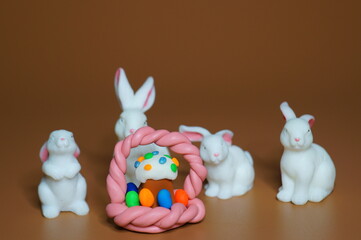 A group of toy rabbits and an Easter cake with a basket of plasticine. Brown background.