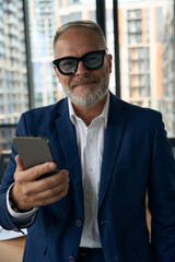 Pleased experienced entrepreneur posing with his smartphone at office
