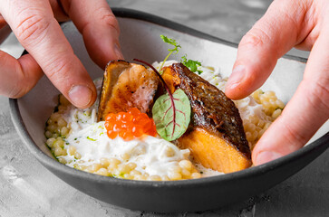 chef hand cooking grilled salmon fish fillet with creamy ptitim, cheese and caviar