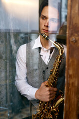Obraz na płótnie Canvas Young man saxophonist with instrument view from window