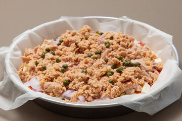 Uncooked homemade Italian pizza with tuna, onions and capers on baking paper (selective focus)