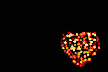 Defocused red and yellow confetti in the shape of a heart with bokeh effect on a black background with copy space (backdrop for Valentines Day)