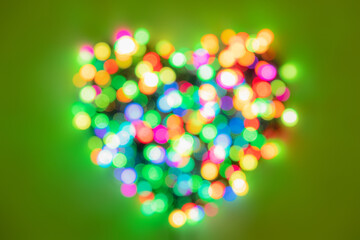 Heart shape made of multi-colored circles of lights on bright green background. Flat lay background...