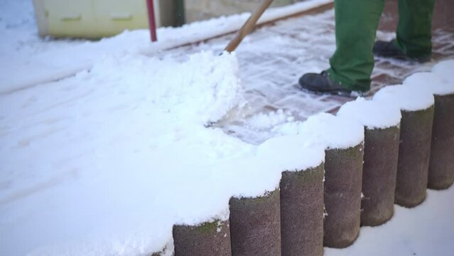 A worker in green work clothes clears snow from a private property in the city.