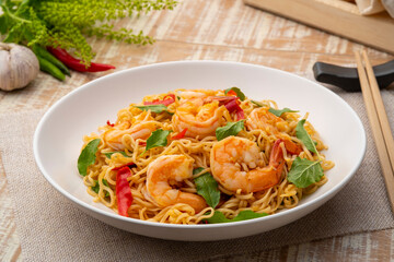 Spicy stir fried instant noodle with shrimps and thai basil leaves in white plate