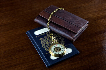 Vintage UK Pasport with Leather Wallet and Old Pocket Watch on a Wooden Surface - 565607492