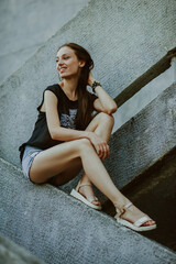Naklejka premium teenage girl with long hair poses; slender figure of a beautiful girl with emotional facial expressions; sunglasses on the head; a person against the background of a city landscape;