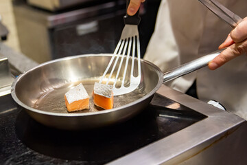 man chef cooking fried salmon fish in frying pan on kitchen