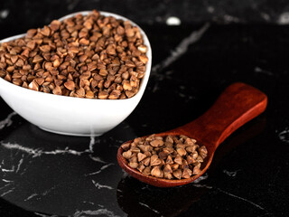 A small wooden spoon and a heart-shaped plate with buckwheat and on a beautiful marble surface.