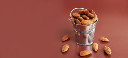 A small metal bucket filled with dried almond kernels on a brown background.