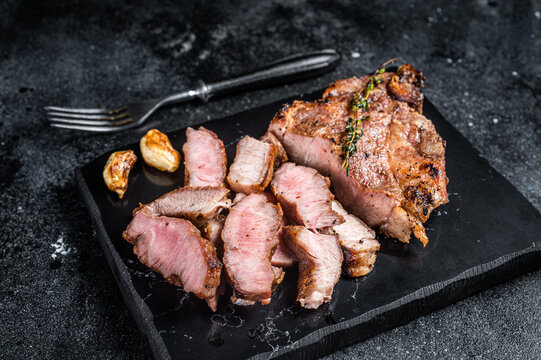 Grilled sliced pork loin steak on marble board. Black background. Top view