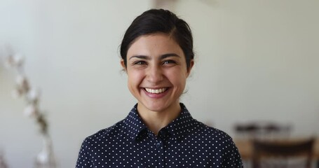 Portrait of beautiful young Indian woman wearing casual shirt, looking at camera with toothy smile, turning facial expression from serious to happy, laughing, posing indoors. Front head shot - Powered by Adobe