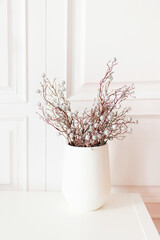 Soft home decor, white vase, vase with decorative branches with silver balls on a white wall background. Interior.