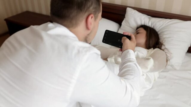 Couple love taking a phone selfie portrait while relaxing in their bedroom together for social media at home. Happy young man and woman smile when taking pictures before posting on online apps