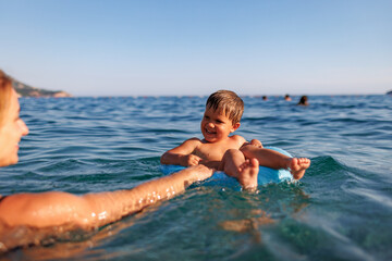 Caring mother rides her son on an inflatable ring in the sea