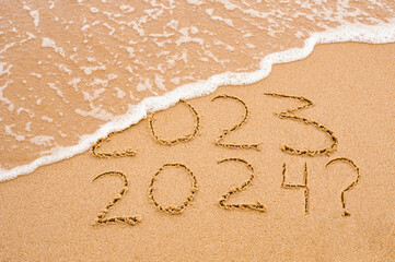 Inscription 2023 and 2024 numbers written on sand with question mark. Concept image