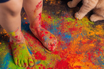 children's feet strewn with multi-colored bright Holi colors and cat paws nearby, copy space....