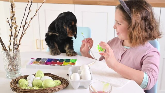 Little girl paints eggs for Easter. Child schoolboy of European appearance and Easter eggs, decor on the table. Light interior and natural shots. High quality 4k footage