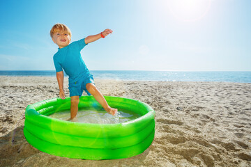 Little boy stand playing inflatable pool over sea at beach