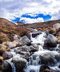 Obraz premium Stream rushing over rocks in Cairngorms National Park, Scotland, popular hiking and skiing area. A tall peak rises in the distance, snow on one face.