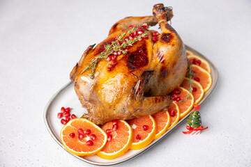 Chicken baked whole to appetizing crispy crust with pomegranate and red orange. Traditional New Year and Christmas dish. Next to a miniature Christmas tree. Close-up, selective focus.