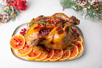 Chicken baked whole to appetizing crispy crust with pomegranate and red orange. Traditional New Year and Christmas dish. In the background are Christmas decorations. Close-up, selective focus.