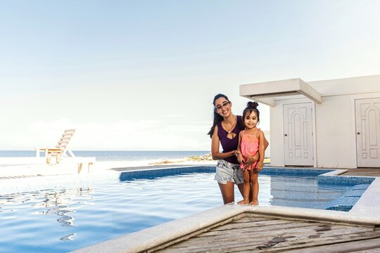 Young hispanic mother with baby daughter together in swimming pool.